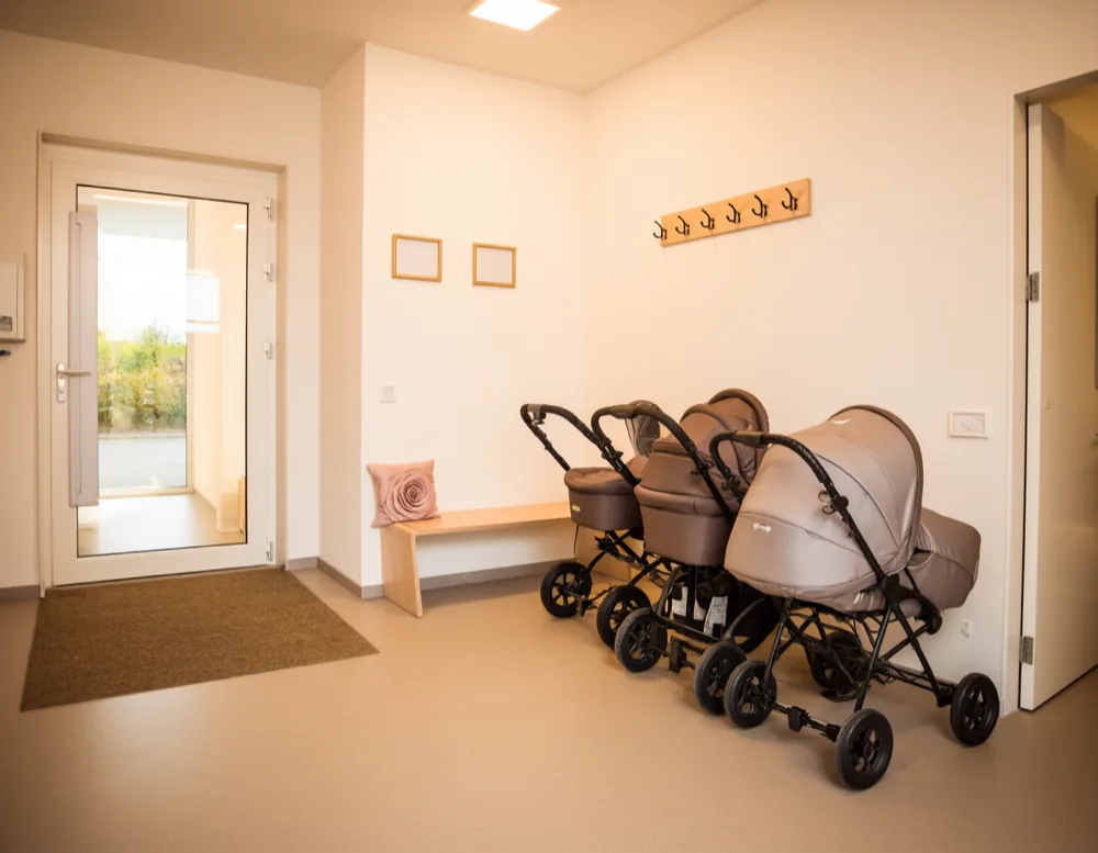 The entrance hall with four prams parked along the wall, a wooden bench with a rose cushion and a row of coat hooks